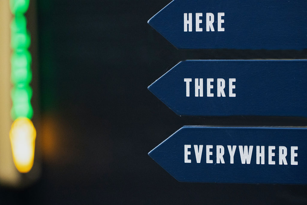 Photo illustration of directional signs labeled here, there, and everywhere by Nick Fewings, Unsplash