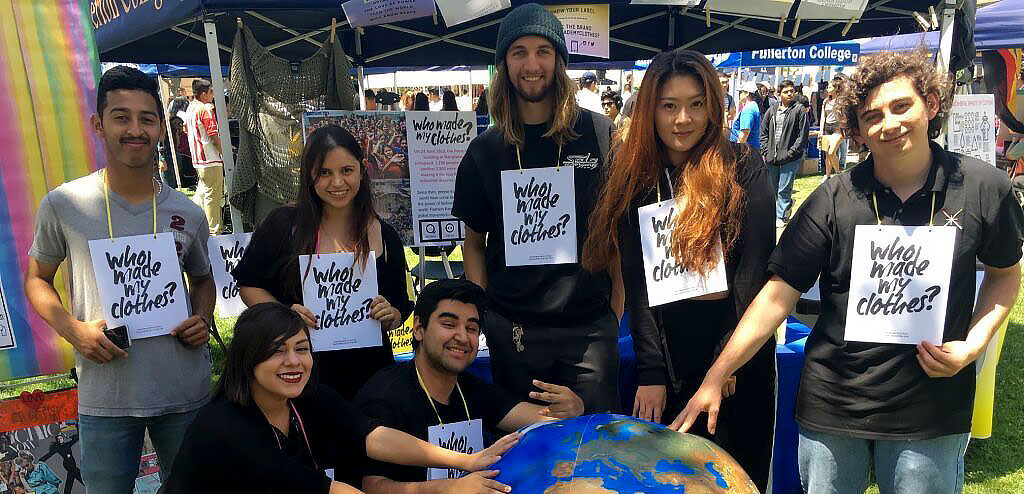 Photo of Fullerton College geography students attending a fair pose with a large globe and hold signs saying "Who made my clothes?". Courtesy Fullerton College