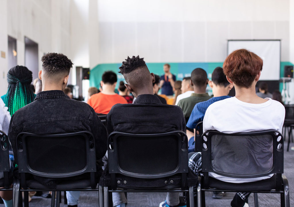 Image of diverse group of students seated in a classroom and listening to a lecture, by Sam Balye for Unsplash