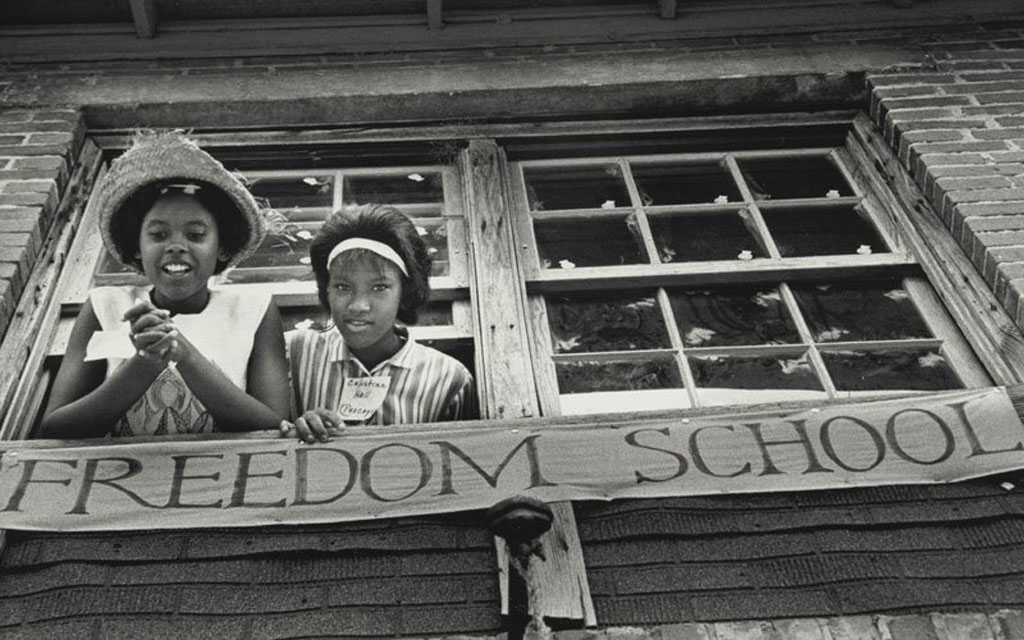 Two young African-American girls look down from window in front of the Freedom School Photo by Ken Thompson, ©The General Board of Global Ministries of The United Methodist Church, Inc. Used with permission of Global Ministries.